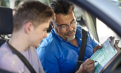 Fahrlehrer und Fahrschüler gehen im Auto gemeinsam die Unterlagen durch